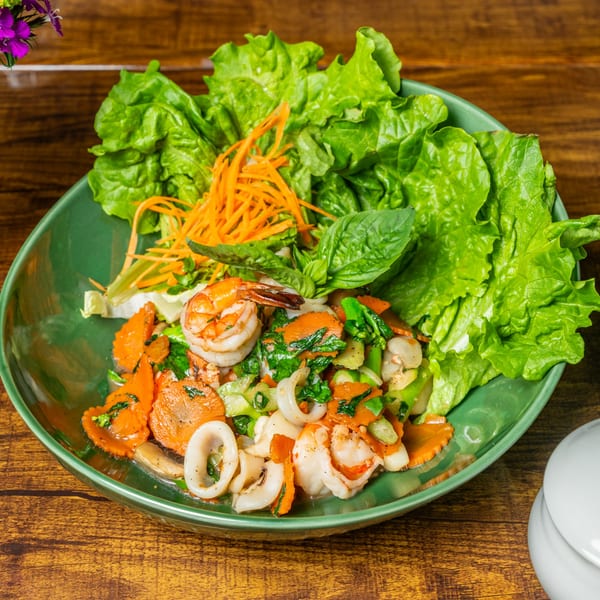 Thai stir-fried seafood with carrots, green vegetables, and fresh lettuce on a green plate.