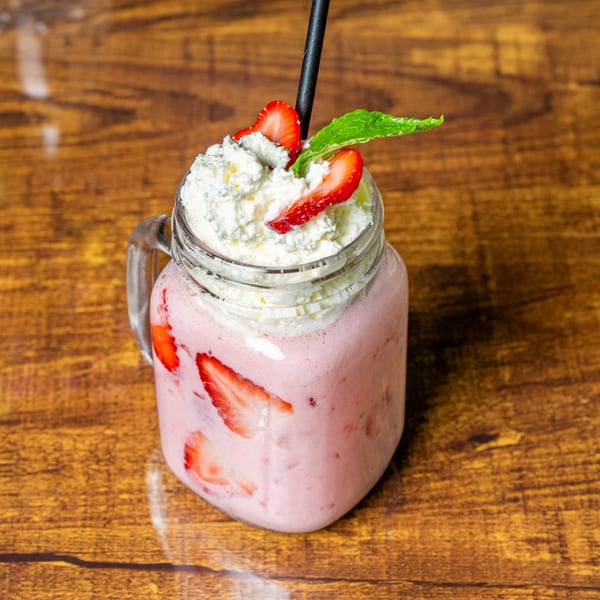 Strawberry smoothie with whipped cream, fresh strawberries, and a mint leaf on a wooden table.