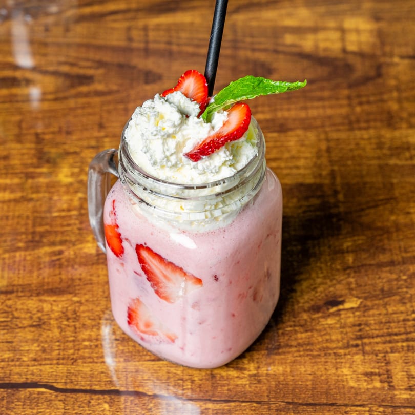 Strawberry smoothie with whipped cream, fresh strawberries, and a mint leaf on a wooden table.
