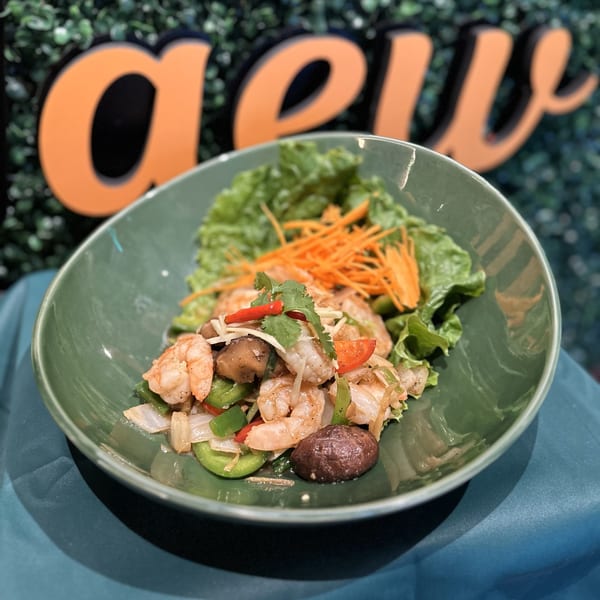 A vibrant Thai shrimp dish with bell peppers, mushrooms, and lettuce in a green bowl.