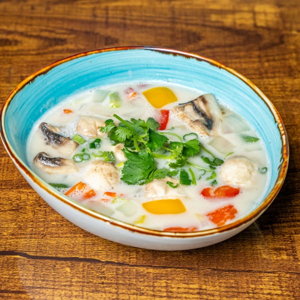 Creamy Thai soup with mushrooms, bell peppers, and cilantro in a blue bowl on a wooden table.