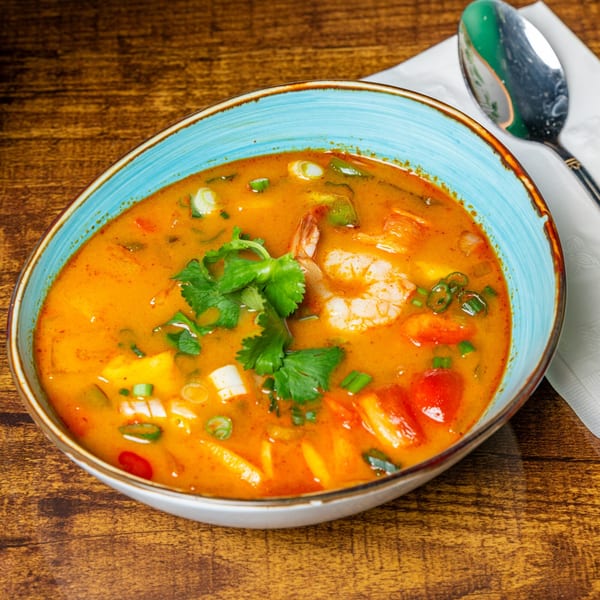 A vibrant orange Thai soup with shrimp, vegetables, and cilantro in a blue bowl.