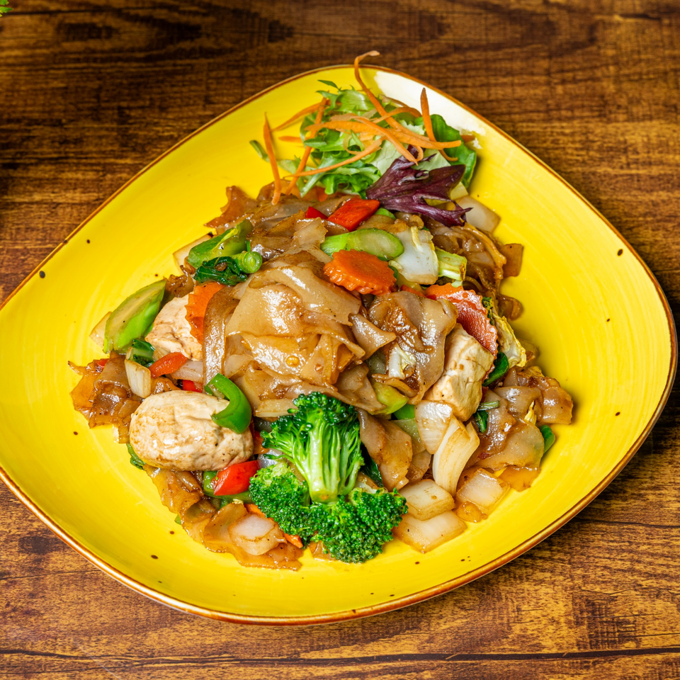 Jaew Thai Cuisine's Pad See Ew with wide noodles, chicken, broccoli, and mixed vegetables on a yellow plate.