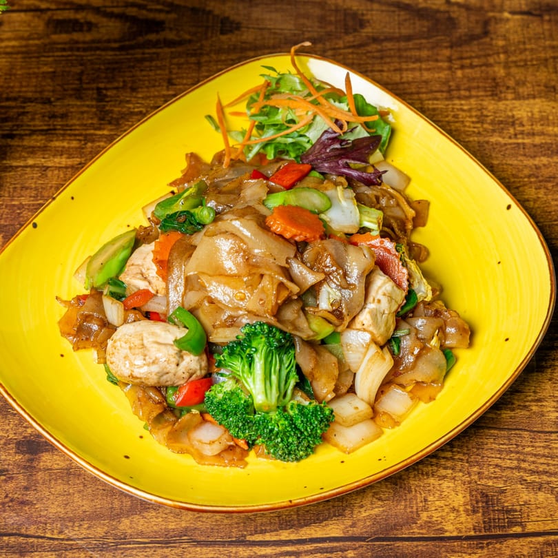 Jaew Thai Cuisine's Pad See Ew with wide noodles, chicken, broccoli, and mixed vegetables on a yellow plate.