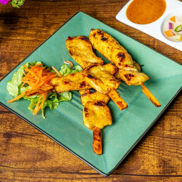 Grilled chicken satay skewers with lettuce, shredded carrots, and peanut sauce on a green plate.